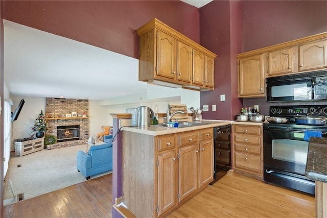 kitchen with a sink, a fireplace, light wood-style flooring, open floor plan, and black appliances