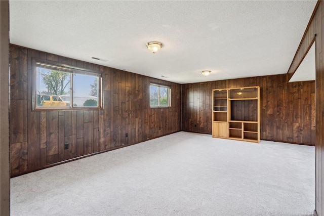 carpeted empty room with wood walls, a textured ceiling, and visible vents