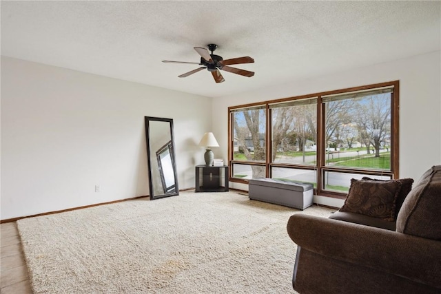 sitting room with a ceiling fan, baseboards, light colored carpet, and a textured ceiling