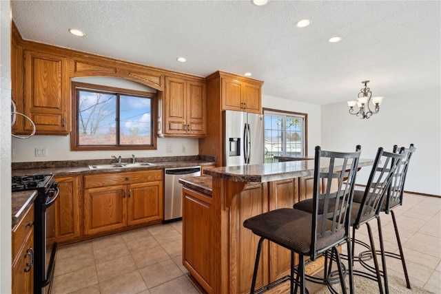 kitchen featuring brown cabinetry, a sink, dark countertops, and stainless steel appliances