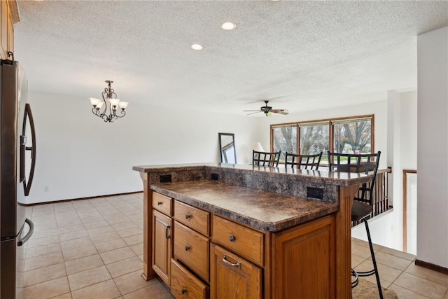 kitchen with stainless steel fridge, a breakfast bar area, ceiling fan with notable chandelier, and dark countertops