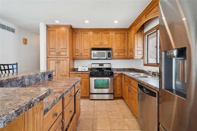 kitchen featuring brown cabinets, dark countertops, appliances with stainless steel finishes, a sink, and visible vents