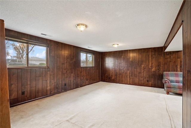 carpeted spare room featuring visible vents, wood walls, and a textured ceiling
