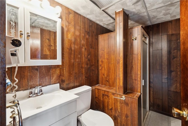 bathroom featuring vanity, a stall shower, wooden walls, and toilet