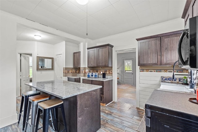 kitchen featuring light stone counters, a breakfast bar, a sink, light wood-style floors, and a center island