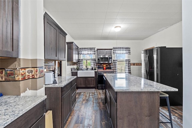 kitchen featuring a kitchen island, appliances with stainless steel finishes, dark brown cabinets, a sink, and dark wood-style floors