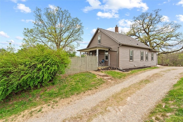exterior space with dirt driveway, fence, and a chimney