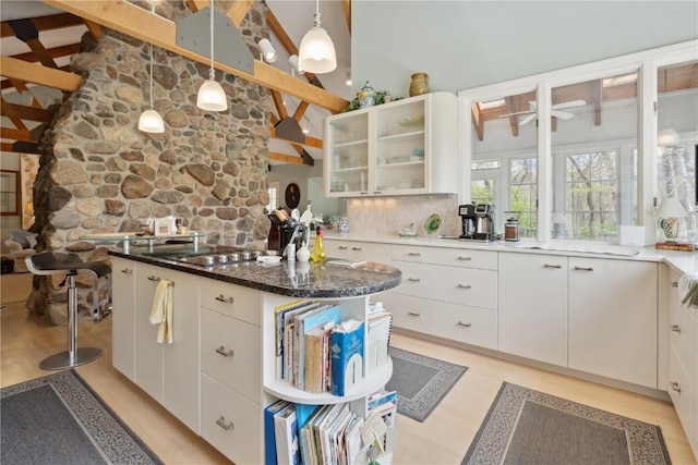 kitchen with a center island, hanging light fixtures, beam ceiling, high vaulted ceiling, and glass insert cabinets