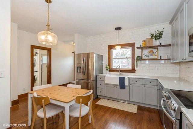kitchen with gray cabinets, stacked washer / drying machine, a sink, dark wood-style floors, and stainless steel appliances