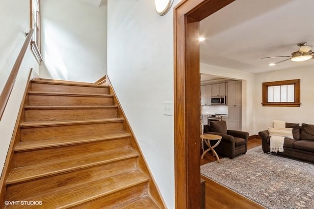 stairway featuring a ceiling fan, baseboards, and wood finished floors