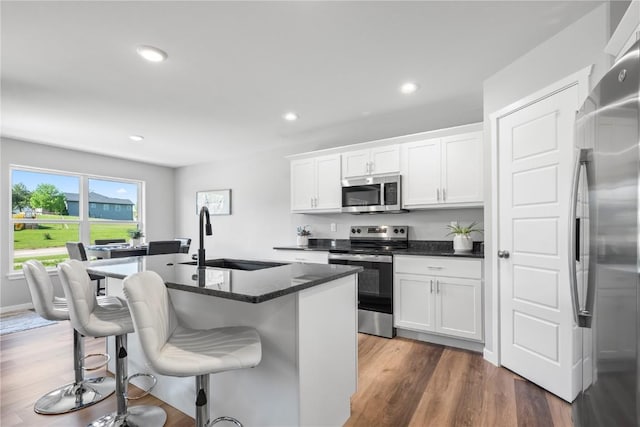 kitchen with stainless steel appliances, a sink, a breakfast bar area, dark wood finished floors, and white cabinetry