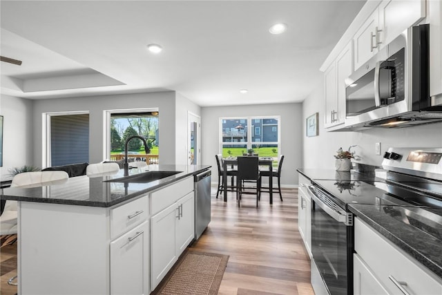 kitchen with stainless steel appliances, a sink, light wood-style flooring, recessed lighting, and dark stone countertops