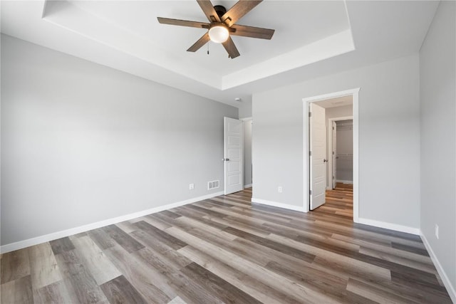 unfurnished bedroom with a raised ceiling, wood finished floors, baseboards, and ceiling fan