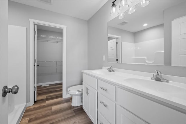 bathroom featuring wood finished floors, toilet, double vanity, a walk in closet, and baseboards
