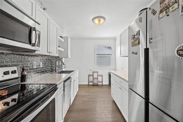kitchen featuring white cabinets, appliances with stainless steel finishes, a sink, wood finished floors, and tasteful backsplash