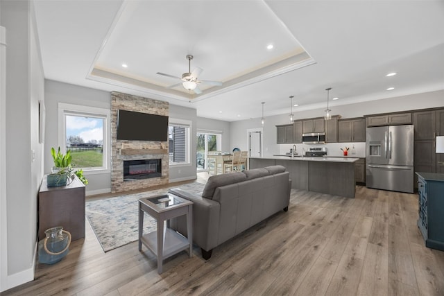 living room with light wood finished floors, a raised ceiling, a fireplace, a ceiling fan, and recessed lighting