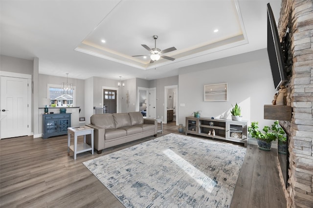 living room featuring a tray ceiling, wood finished floors, ceiling fan with notable chandelier, and a fireplace