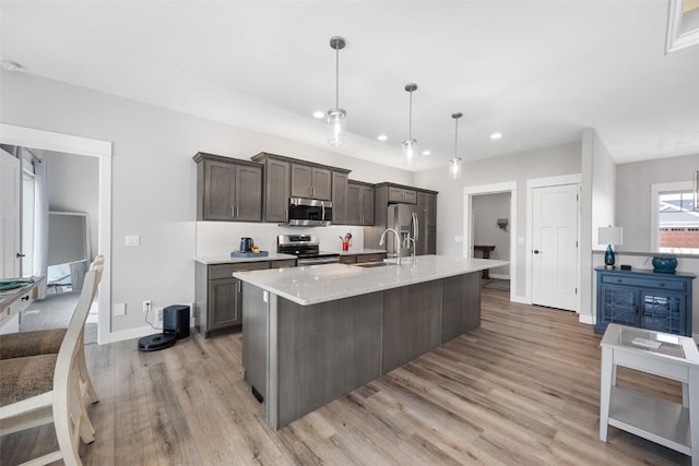 kitchen featuring a kitchen island with sink, dark brown cabinetry, light wood-type flooring, a sink, and stainless steel appliances