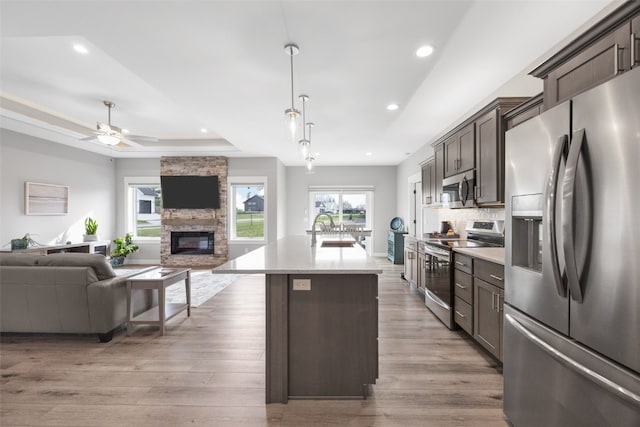 kitchen with a fireplace, open floor plan, recessed lighting, a tray ceiling, and stainless steel appliances