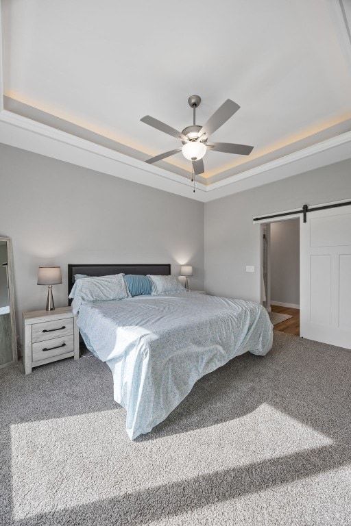 carpeted bedroom with a tray ceiling, a barn door, and ceiling fan