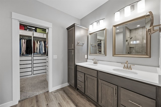 bathroom with a walk in closet, a tile shower, a sink, and wood finished floors