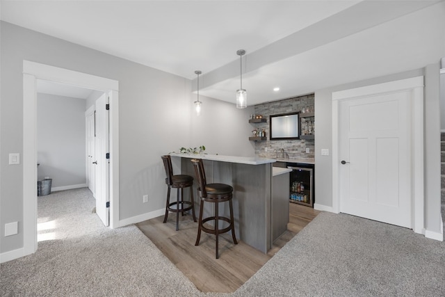 kitchen with a kitchen bar, pendant lighting, light wood-type flooring, a peninsula, and beverage cooler