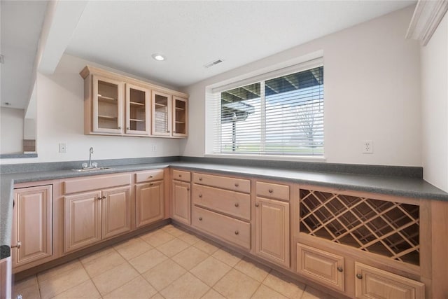 kitchen featuring dark countertops, a sink, glass insert cabinets, light brown cabinets, and light tile patterned flooring