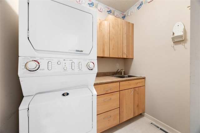 clothes washing area with stacked washer / dryer, visible vents, cabinet space, a sink, and baseboards