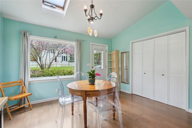 dining area featuring baseboards, a notable chandelier, wood finished floors, and vaulted ceiling with skylight