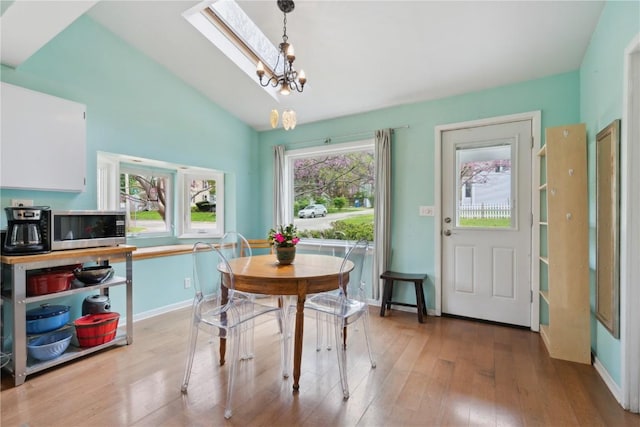 dining space featuring baseboards, a chandelier, light wood finished floors, and vaulted ceiling with skylight