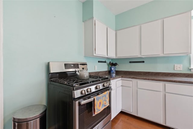 kitchen featuring light wood-style floors, dark countertops, stainless steel range with gas cooktop, and white cabinetry