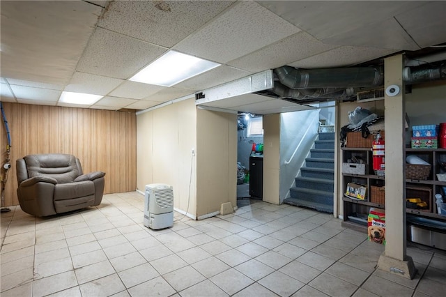 finished basement with stairs, a drop ceiling, and light tile patterned floors