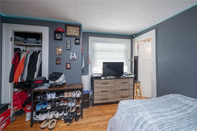 bedroom with a textured wall, wood finished floors, and a closet