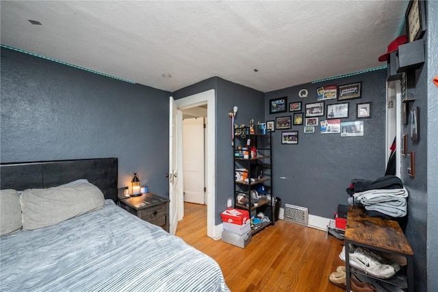 bedroom featuring visible vents, a textured wall, baseboards, a textured ceiling, and light wood finished floors