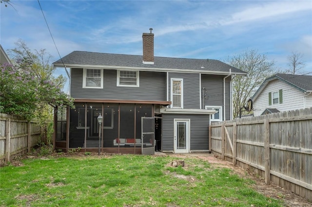 back of house featuring a lawn, a chimney, a sunroom, and a fenced backyard