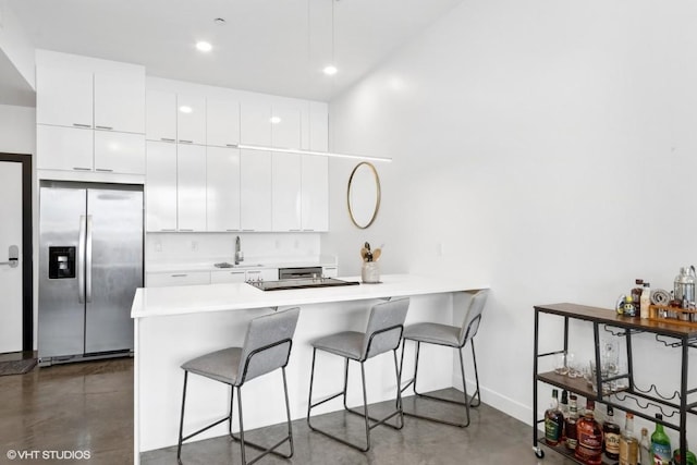 kitchen with a peninsula, stainless steel fridge with ice dispenser, a breakfast bar area, and concrete floors