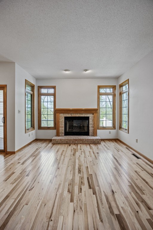 unfurnished living room featuring light wood-style flooring, a textured ceiling, and a wealth of natural light