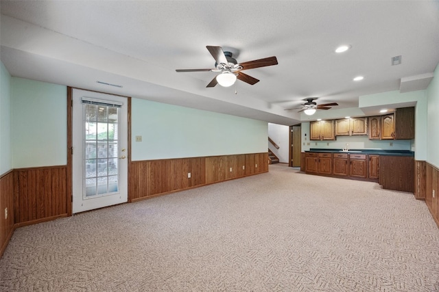 unfurnished living room with light colored carpet, wood walls, a wainscoted wall, stairs, and wet bar
