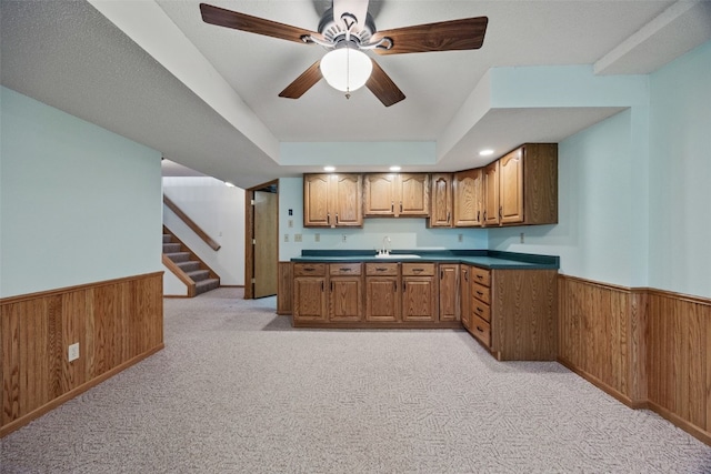 kitchen with wooden walls, brown cabinetry, light carpet, and a wainscoted wall