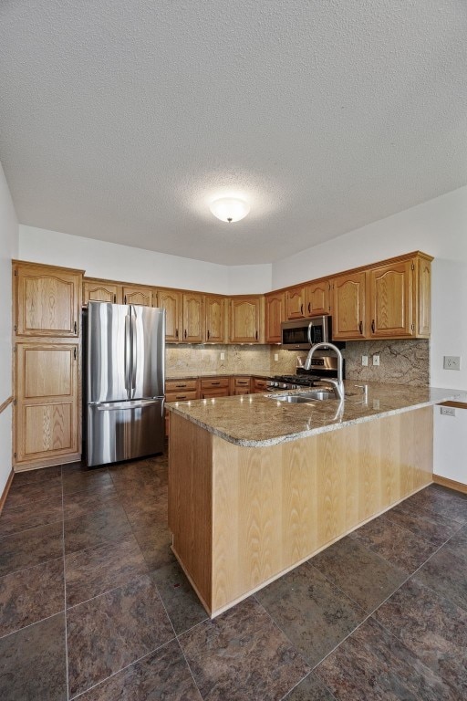 kitchen featuring backsplash, a sink, light stone counters, a peninsula, and stainless steel appliances
