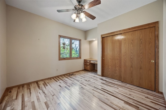 unfurnished bedroom with ceiling fan, built in desk, baseboards, a closet, and light wood finished floors
