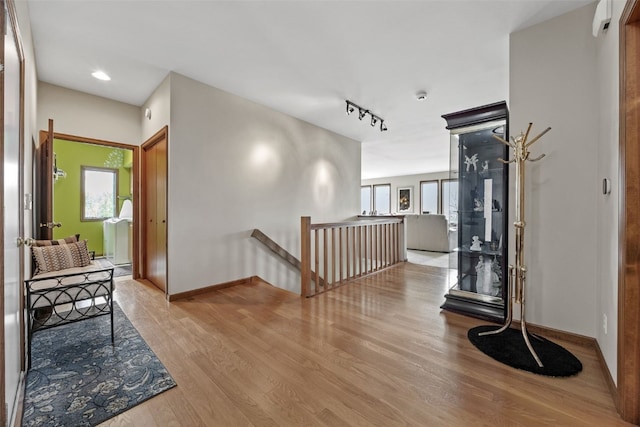 hallway featuring rail lighting, wood finished floors, baseboards, an upstairs landing, and recessed lighting