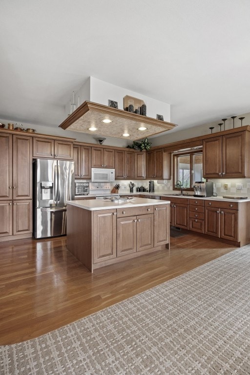 kitchen featuring a center island, wood finished floors, light countertops, stainless steel fridge with ice dispenser, and white microwave