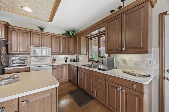 kitchen featuring decorative backsplash, white appliances, light wood-style floors, light countertops, and a sink