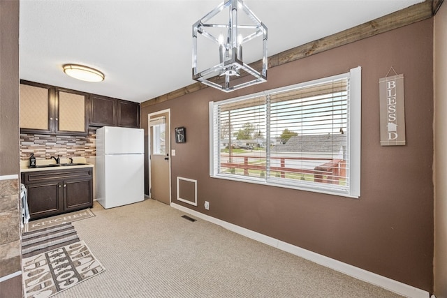 kitchen featuring visible vents, light colored carpet, dark brown cabinets, freestanding refrigerator, and an inviting chandelier