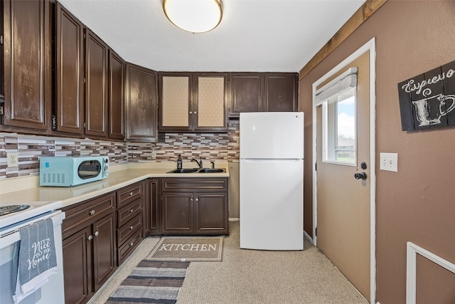 kitchen featuring dark brown cabinetry, a sink, white appliances, light countertops, and backsplash