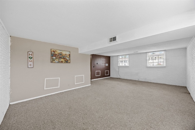 basement with visible vents, carpet flooring, baseboards, and brick wall
