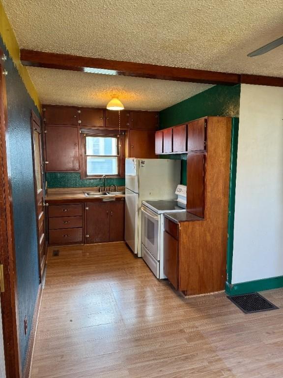 kitchen with electric range, a sink, light wood finished floors, beam ceiling, and a textured ceiling