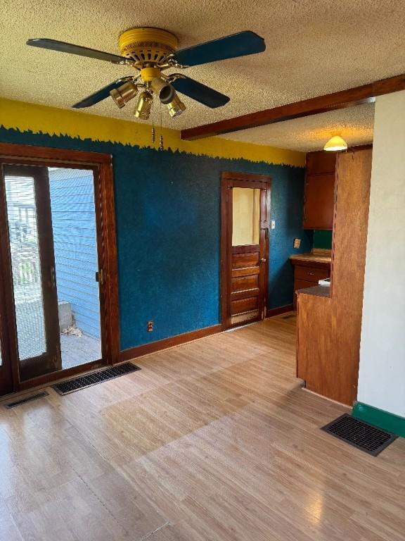 unfurnished living room with light wood-type flooring, a textured ceiling, and visible vents