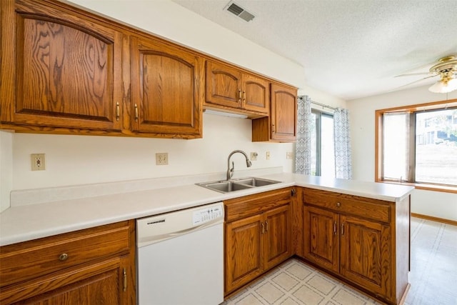 kitchen with white dishwasher, brown cabinetry, a peninsula, and a sink